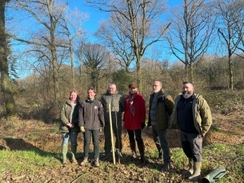 A group of people smiling whilst planting a tree