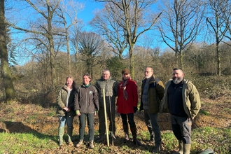 A group of people smiling whilst planting a tree