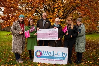 A group of people standing underneath a tree holding a cheque