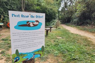 Sign with cartoon Otter (Oscar) and information, grass and path in the background