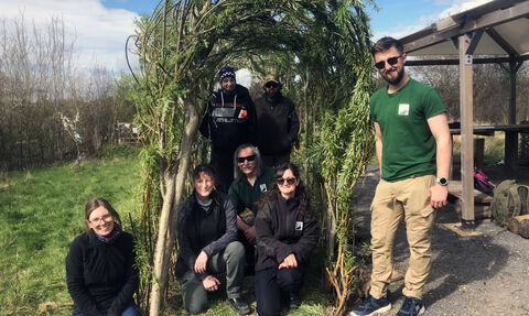 Group of men and women stand and sit under willow arch