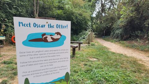 Sign with cartoon Otter (Oscar) and information, grass and path in the background