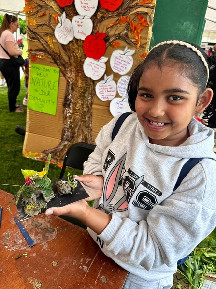 A young Asian girl in a hoodie holding a piece of art created with clay and items from nature. 
