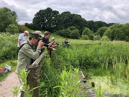 People with binoculars and cameras looking out over a pond