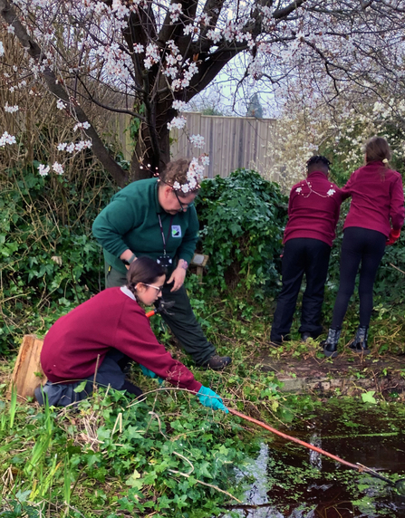 Pupil clears some weeds from pond with help of WWT team member