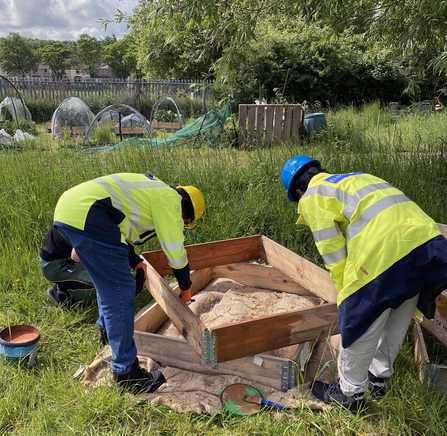 Two volunteers in high vis jackets construct a planter from panels