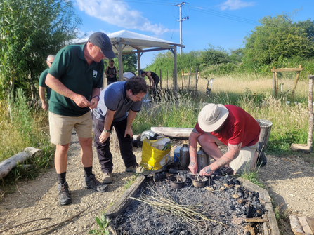 One man lighting a campfire with two men nearby watching