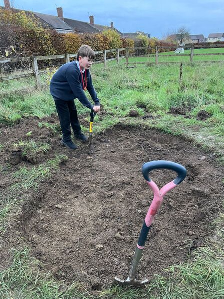 Pupil helping dig a pond in the school field