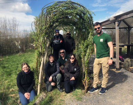 Group of men and women stand and sit under willow arch