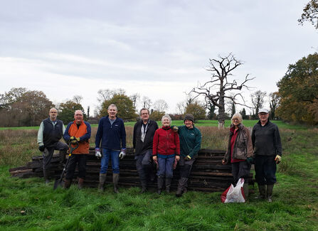 A group of volunteers stand in front of wood pile