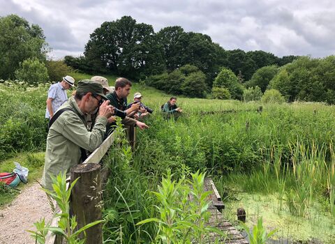 People with binoculars and cameras looking out over a pond