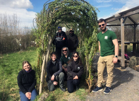 Group of men and women stand and sit under willow arch